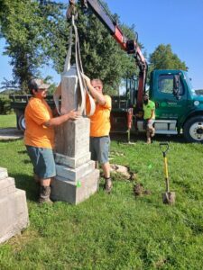 Two men assisting with placing cemetery head stone.